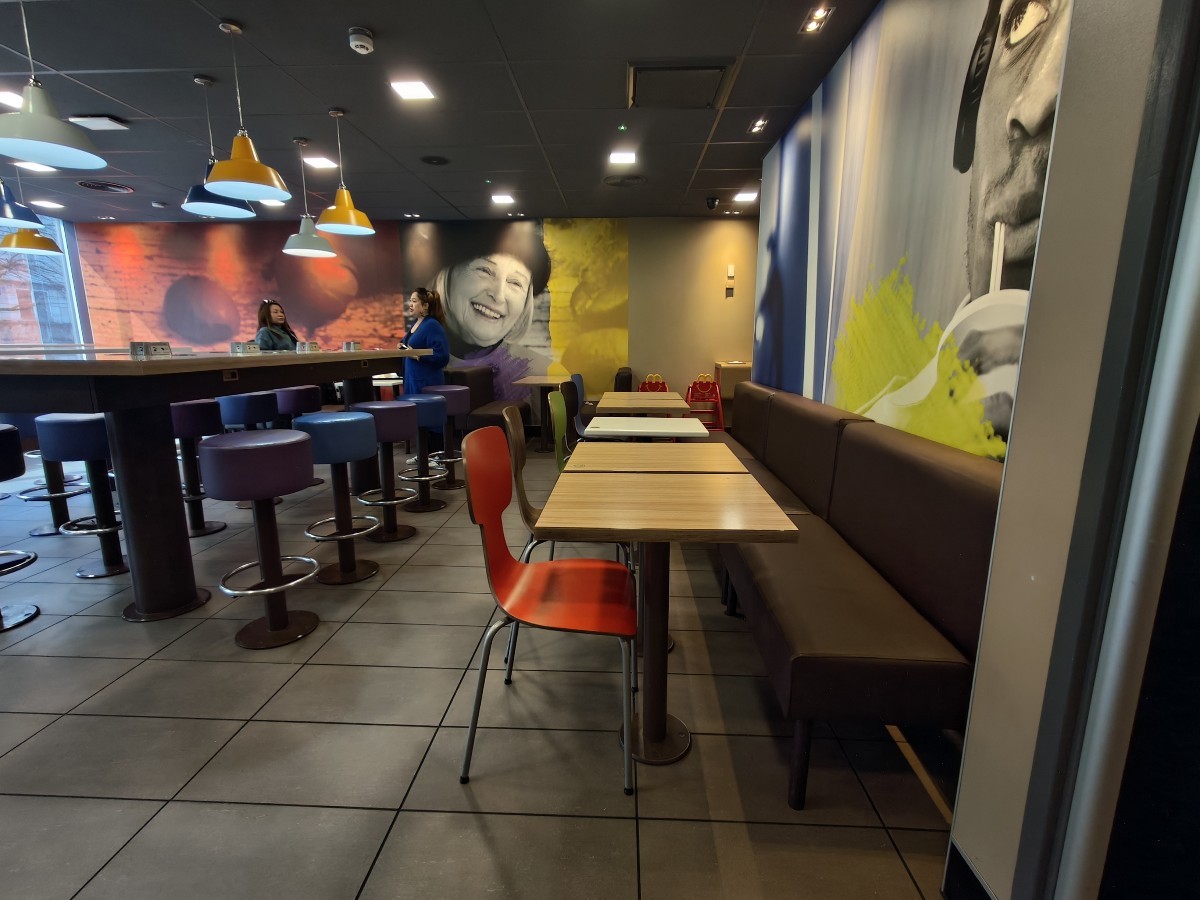From doors facing right. Half booth along centre. Path on left to more seating. High table and stools on back left.