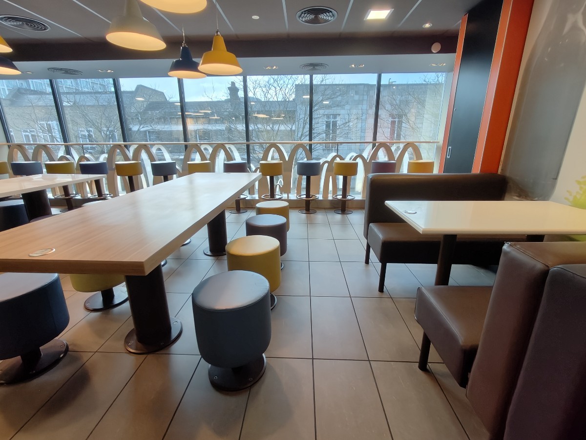 From before booths facing left. Booths along right. Path in centre to high table and stools along back glass wall. Table and stools on left.