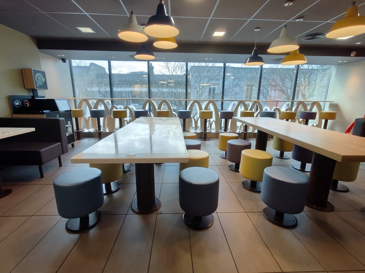 From door facing straight. Booth along left. Table and stools along centre. High table and stools behind along back glass wall.