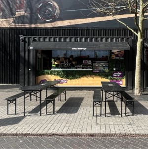 From street facing venue. Tables and benches on left and right. Path in centre to counter at back.