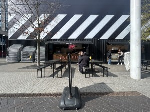 From street facing venue. Standing sign in centre. Path behind to counter at back. Tables and benches on left and right.