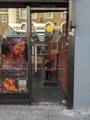 Glass door with black frame and metal handle on left. Push to open.