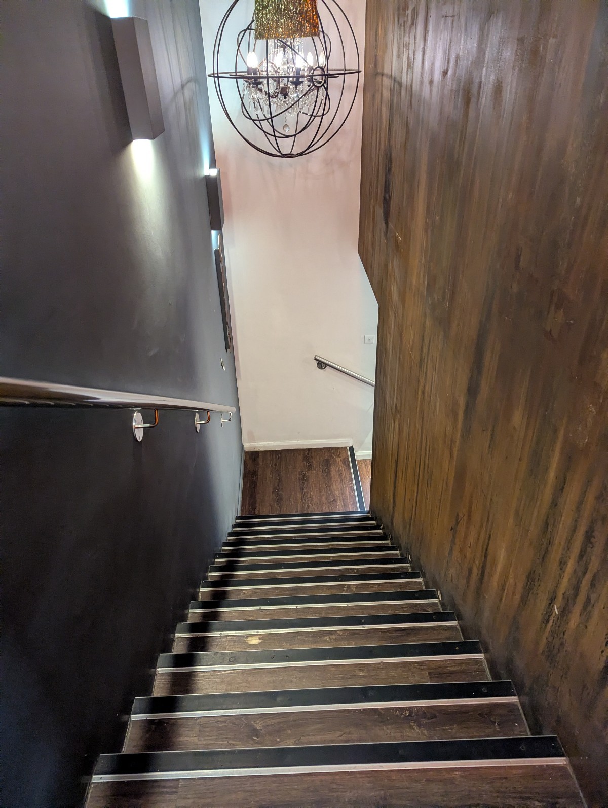 Stairs to Oblo are very dark with wood one wall and black paint on the other. Silver handrail and wood stairs with black & silver strip on each stair.