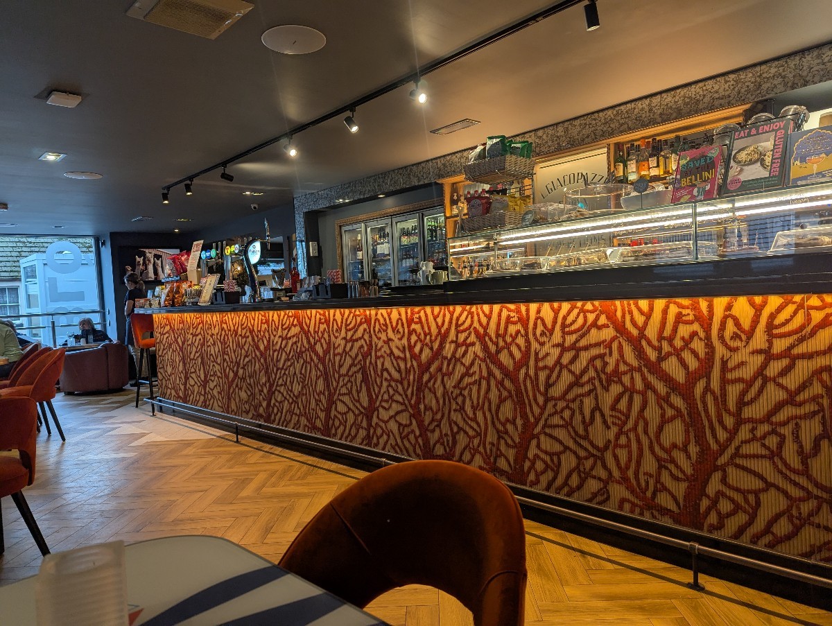Counter area with bar and glass cake display. Some low comfy seats. Around the corner is a conservatory and entrance to toilets.