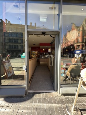Glass door with grey frame. Silver handle to left of door, push to open if automatic door is not working. Doorbell to left.