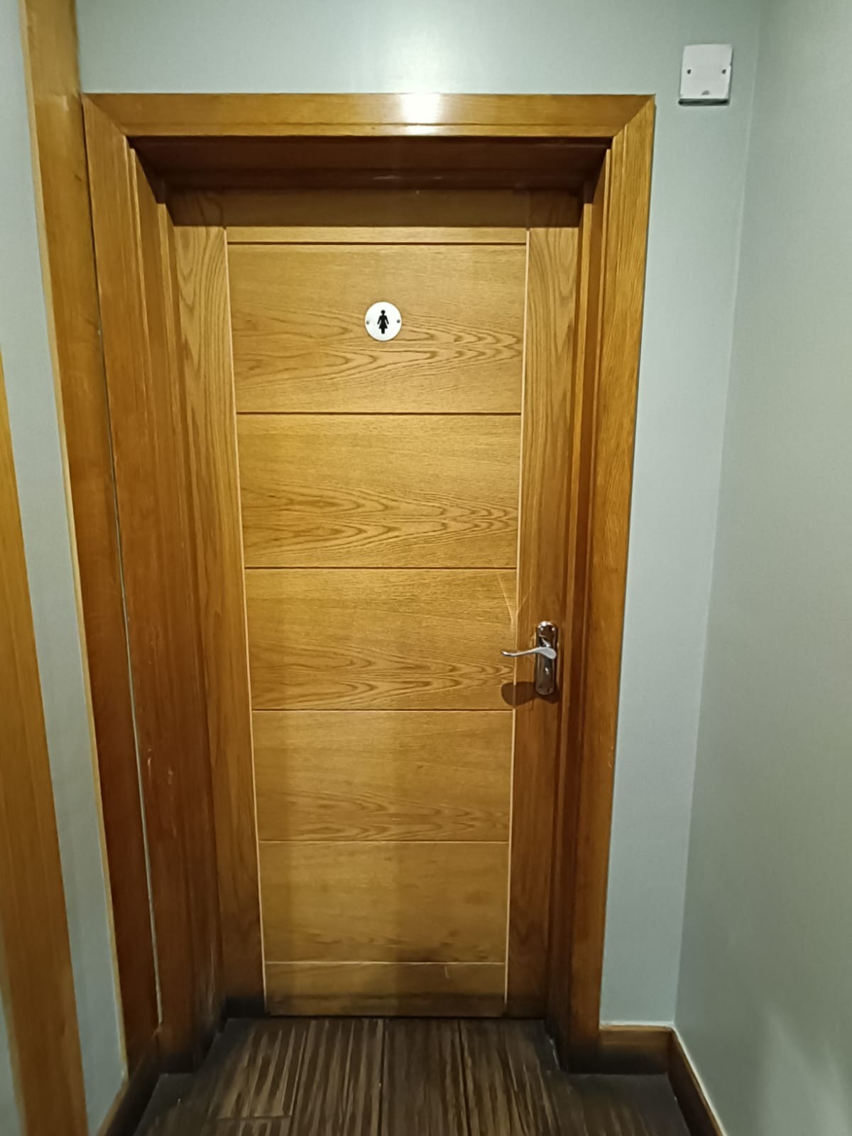 From end of path after archway facing straight. Wooden toilet door ahead. Push silver handle on right to open.