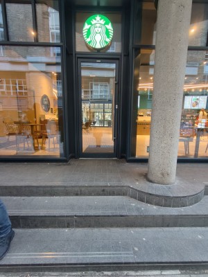 Facing entrance. Three steps up to door. Black framed glass door. Push silver metal handle on right to open.