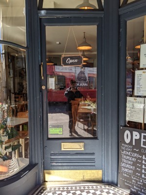 Glass door with green frame and metal handle on left. Push to open.