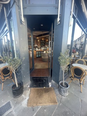 From street facing venue. Opening ahead. Planters on both sides. Built-in ramp up at foot of opening with two doormats on it.