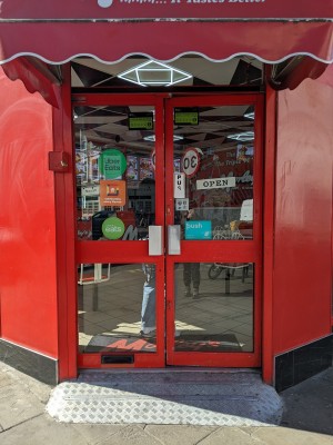 Glass doors with red frame and metal handles in centre. Push to open.