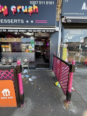 From pavement facing venue. Pink fence along left and right. Path in centre to entrance door at the back.