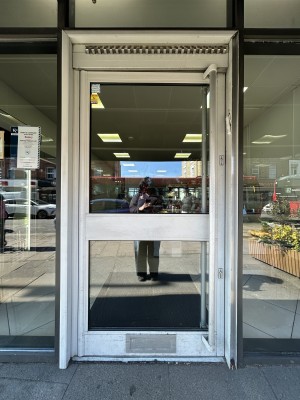 Glass door ahead with light frame. Push silver handle on right to open.