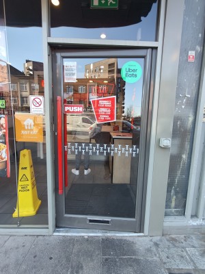 Grey framed glass door. Push red handle on left to open.