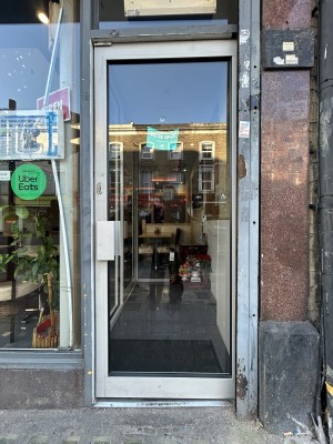 Glass door ahead with light frame. Push silver handle on left to open.