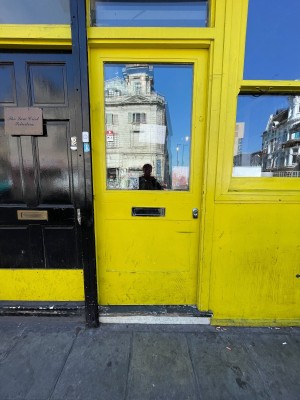Glass door with yellow frame. Push from right to open.