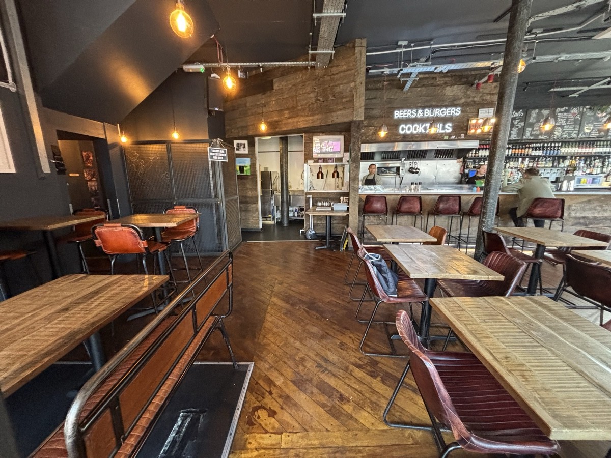 From entrance left. Tables and benches on left. High tables and stools and back left. Tables and chairs on right. Bar counter on back right.
