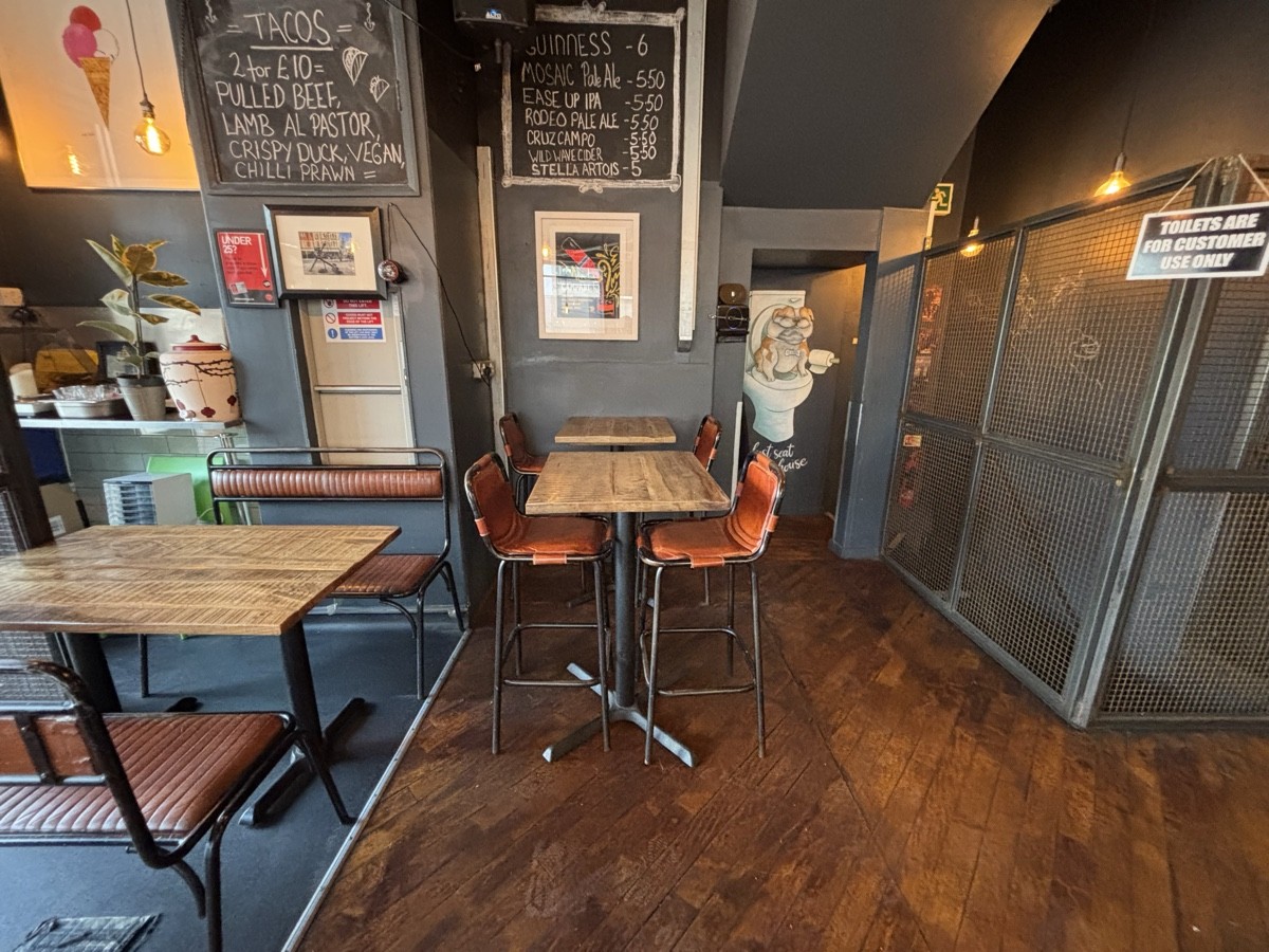 From end of bench facing left. Tables and benches on left. High tables and stools ahead. Path on right to toilet downstairs.