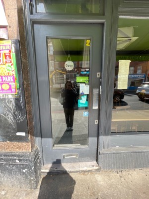 Facing glass door with gray frame. Push on right to open.