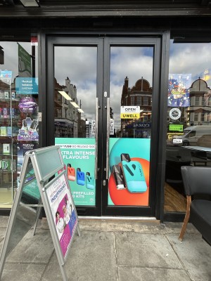 Glass doors ahead with black frame. Push silver handles in centre to open. A-frame sign on left obstructs left door.