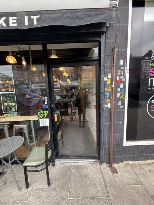 Glass door with black frame. Push via handle on left to open.