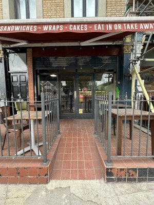 From pavement facing venue. Ramp ahead. Grey railings to left and right of it.