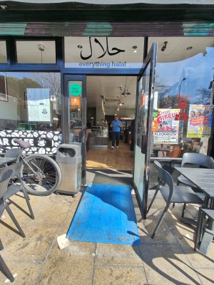 Ramp upon request to black framed glass door. Pull black handle on left to open.