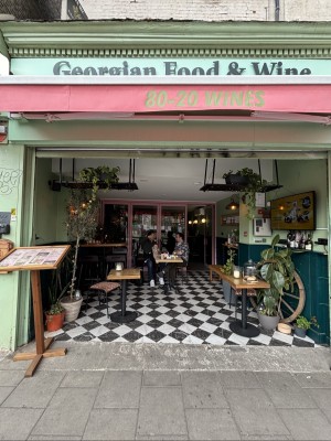 From pavement facing venue. Opening ahead. Outdoor seating behind along left. Entrance door to back right.