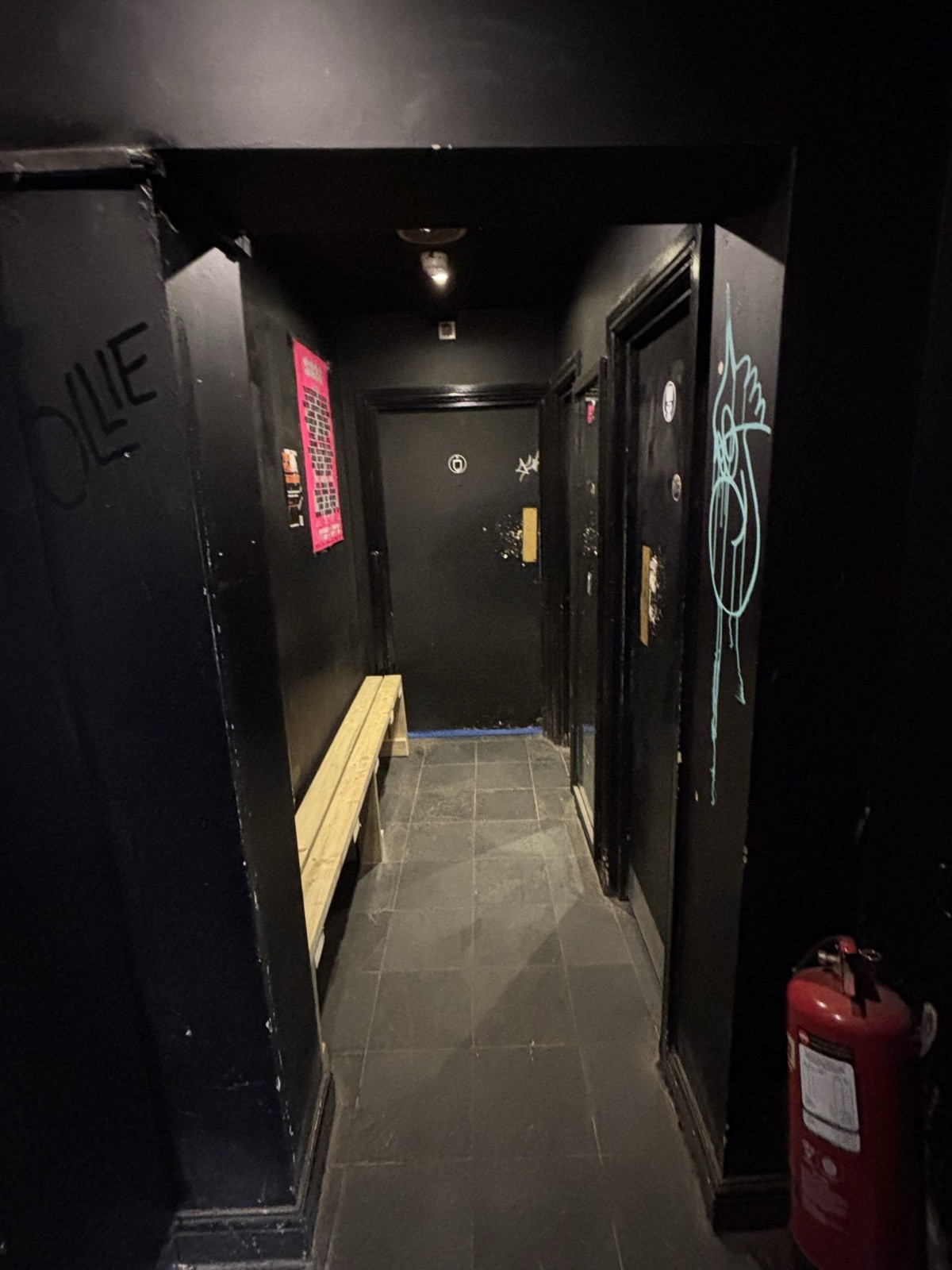 From preceding door facing left. Open archway ahead. Bench behind along left. Urinals on back. Cubicles along right.