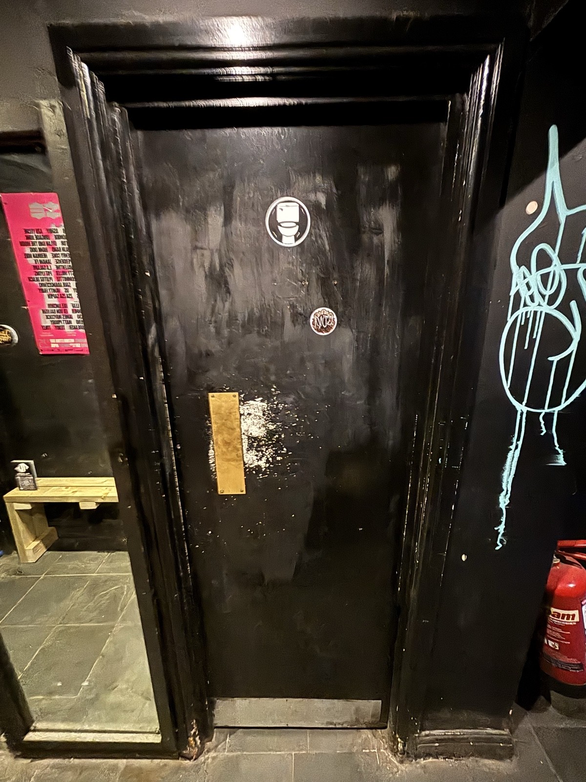 From archway facing right. Black door ahead. Push via brass pad on left to open.