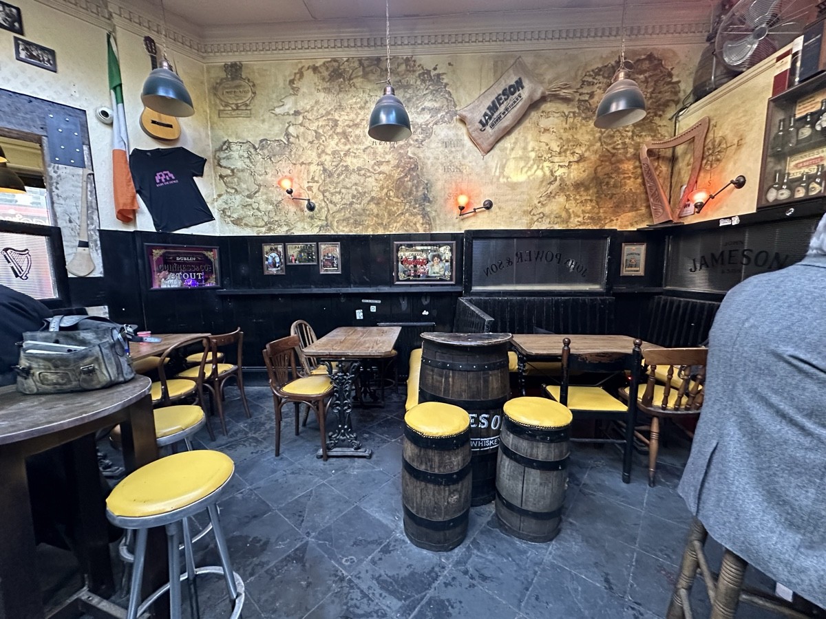 From end of bar facing left. High tables and stools to left and right. Tables and chairs along back. Black divider in-between.