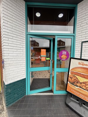 Glass doors with blue frame ahead. Push left door to open via metal handle on right.