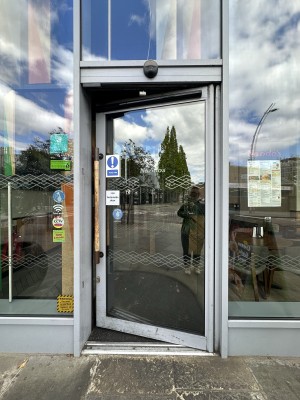 Glass door with grey frame. Push wooden handle from left to open.