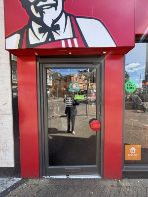 Glass door with black frames. Push red handle on right to open.