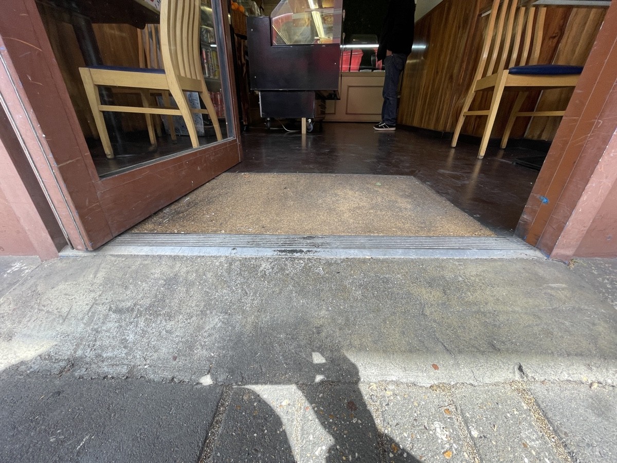 Concrete bump leading up to door. Metal bump at foot of door. Doormat after bump.