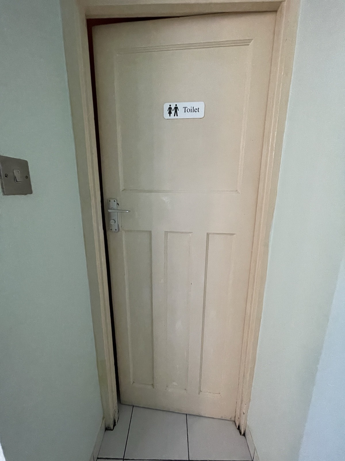 From archway facing left. Bathroom door ahead. White wooden door. Push from silver handle on left to open.