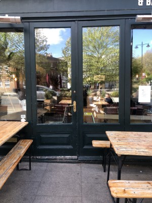 Picnic benches on left and right. Glass doors with dark green frame. Push handle in centre to open.