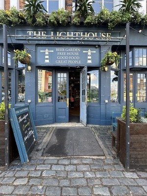 From pavement facing venue. Opening ahead. Planter to right, A-frame to left of it. Centre path leads to entrance doors.