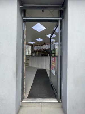 Facing glass door with gray frame. Push sliver handle on left to open.