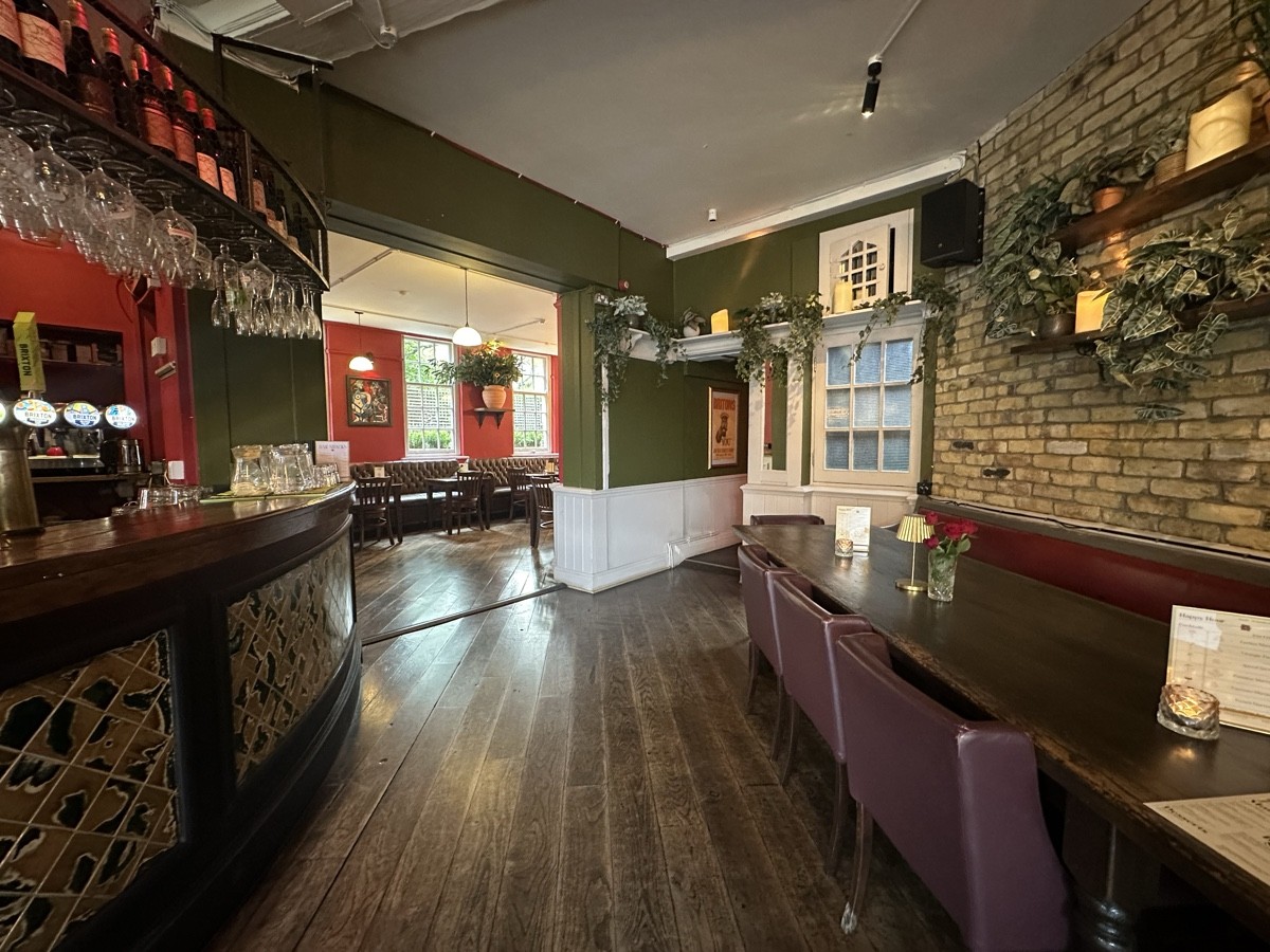 From corner of bar facing straight. Bar continues along left. Open archway to back left to back area. Table and chairs to right. Bathroom behind.