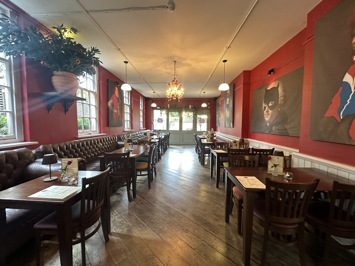 From archway facing right. Half booths along left. Centre path leads to back outdoor area. Tables and chairs along right.
