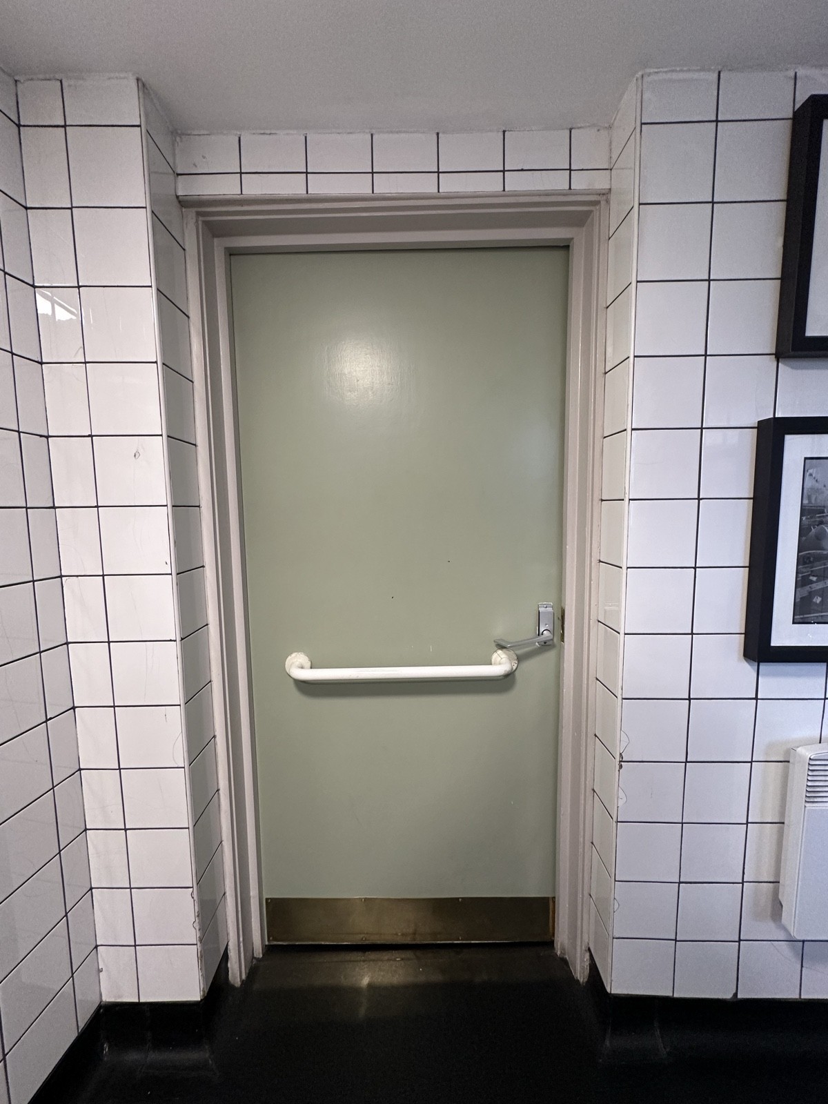 Back of green door. White grab rail in centre. Push silver handle from right to open.