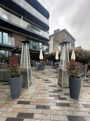 From pavement facing venue. Opening ahead. Planters and heaters to left and right of it.