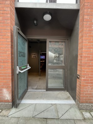 Frosted glass doors with silver frame. Staff need to push door from inside to open. Push button on right for assistance.