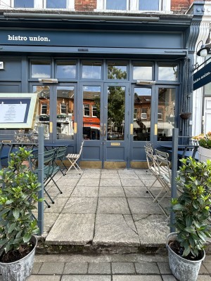 From street facing venue. Opening ahead with blue fence on left and right. Entrance door at back.