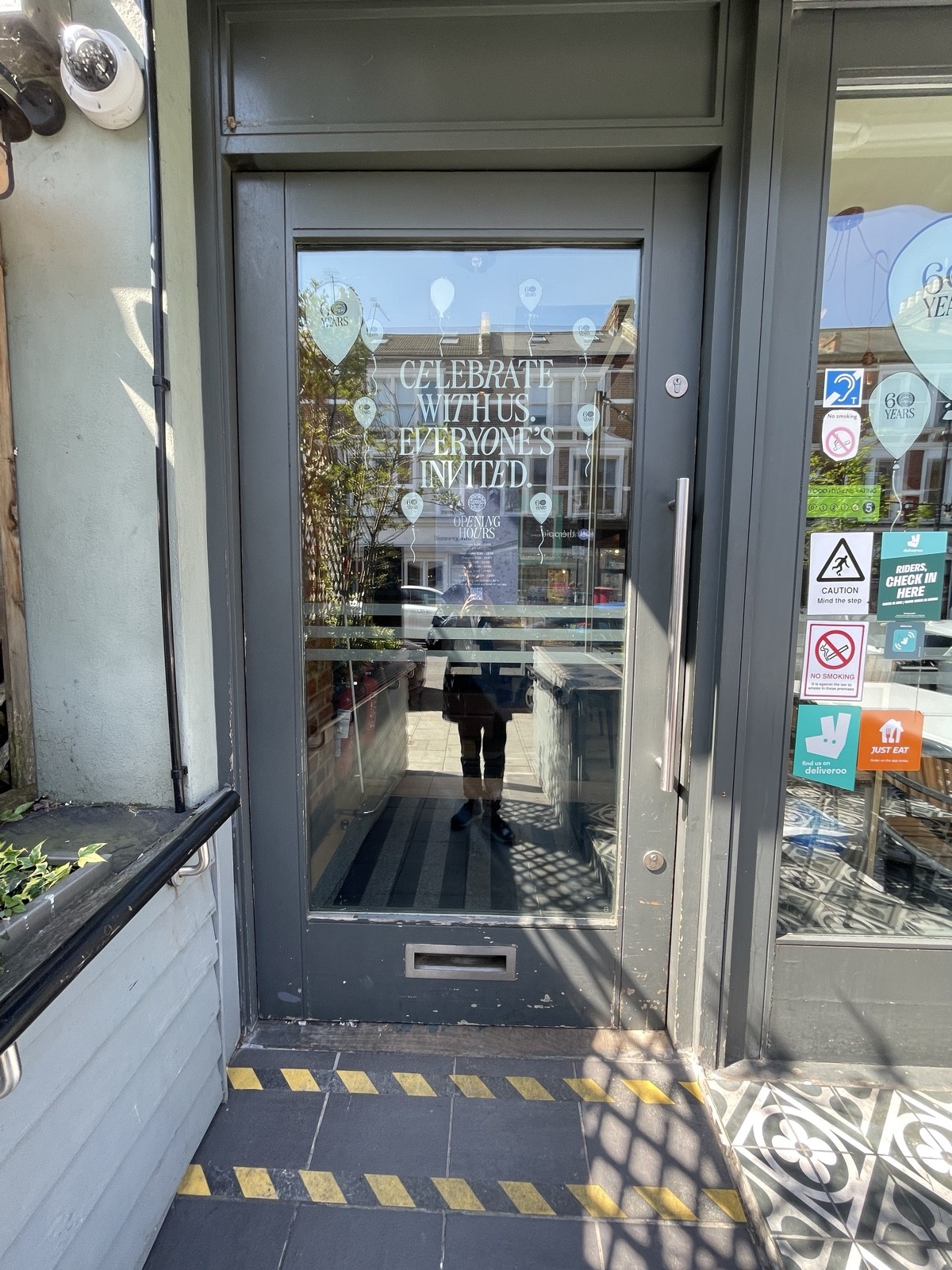 From end of ramp facing straight. Entrance door ahead. Grey wood-framed glass door. Push from metal handle on right to open.