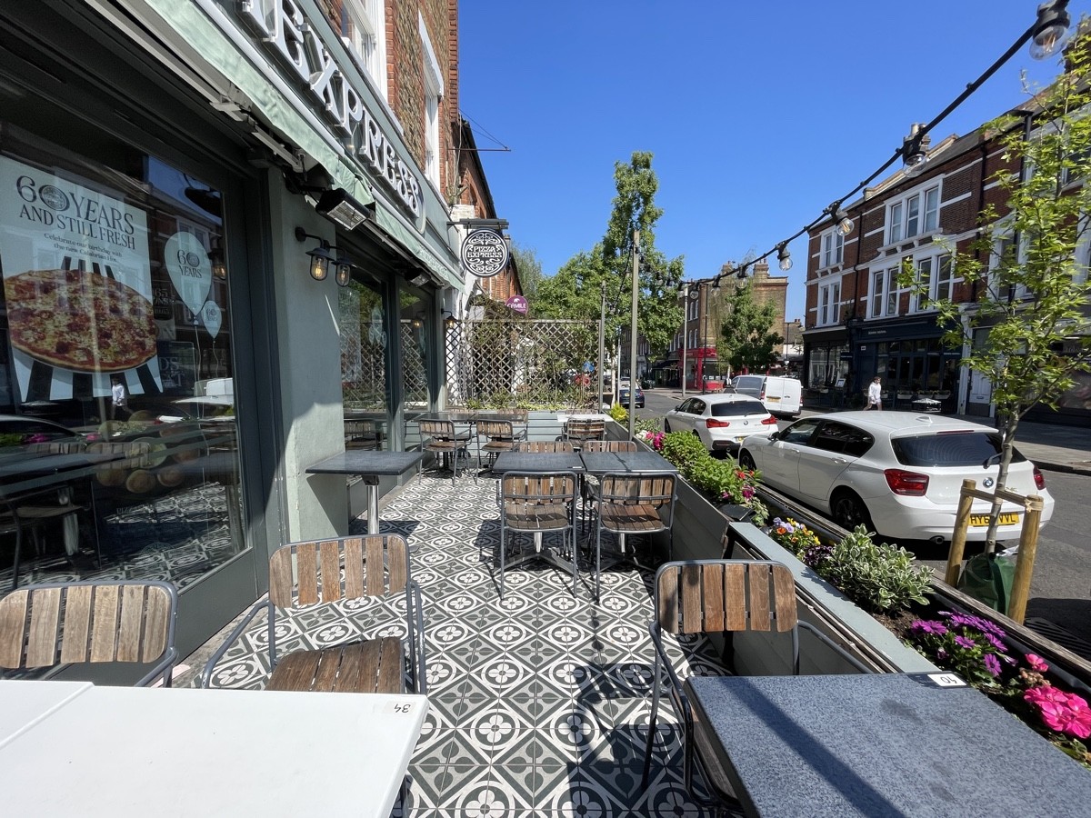 From end of path facing straight. Tables and chairs spread out ahead. Planter along right and back.