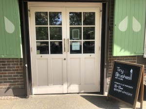 Light pink doors with glass panels. Pull silver handles in centre to open. A-frame sign on right.