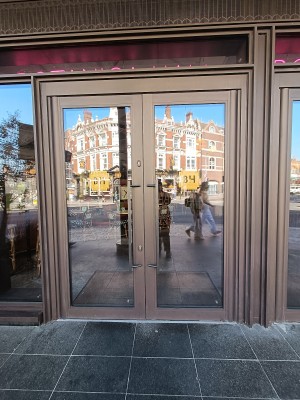 Glass door with brown metal frame. Pull brown, metal handles in middle to open.