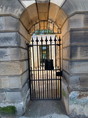 Black gate ahead. Pull from right to open. Path behind to entrance door.