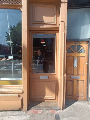 Glass door with brown, wooden frame. Push from left to open.